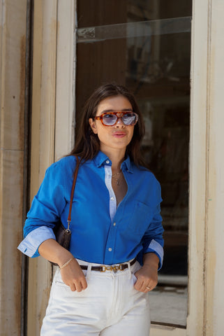 Woman wearing a blue shirt and white pants standing in front of a door.