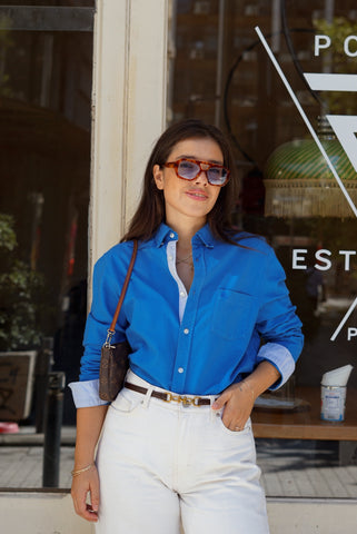Woman wearing a blue shirt and sunglasses standing in front of a store window.