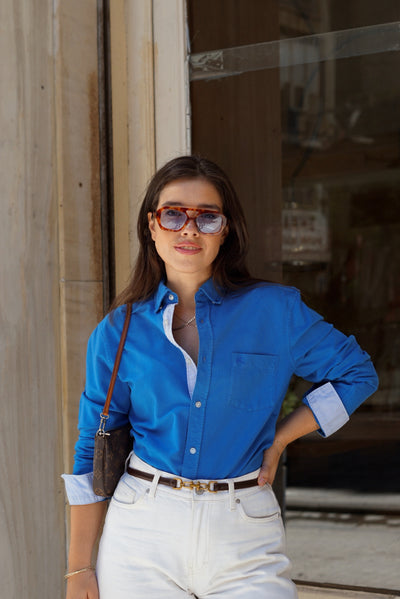 Woman wearing a blue shirt and sunglasses standing in front of a store entrance.