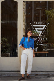 Person wearing a blue shirt and white pants standing in front of a Pozeli pizza restaurant.