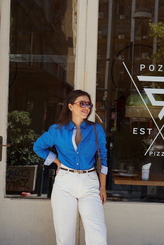 Woman in a blue shirt and white pants standing in front of a store with 'Pozzoli' sign.