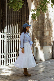 Woman in a blue shirt and white skirt standing in front of a stone wall.