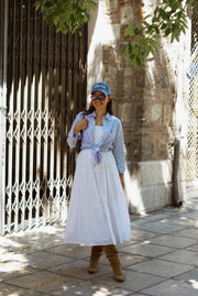 Woman in a white dress and blue shirt standing on a street with a building in the background