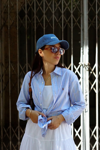 Woman wearing a blue cap and sunglasses, standing in front of a metal gate.