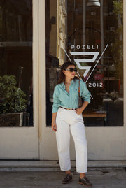 Woman in a light blue shirt and white pants standing in front of a Pozeli store.