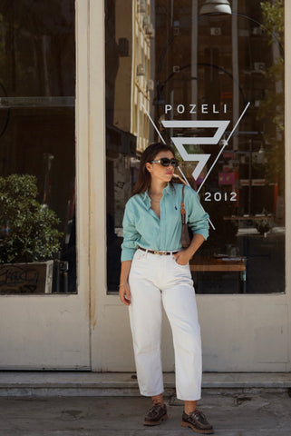 Woman in a light blue shirt and white pants standing in front of a Pozeli store.