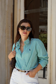 Woman wearing a light blue checkered shirt and white pants, standing outdoors.