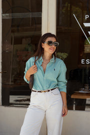 Woman wearing a light blue shirt and white pants standing in front of a store window.
