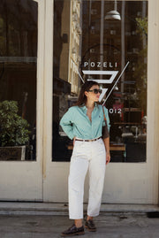 Woman in a light blue shirt and white pants standing in front of a store with 'Pozeli' branding.