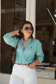 Woman wearing a light blue checkered shirt and white pants outdoors.
