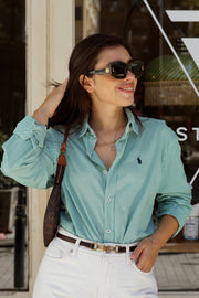 Woman wearing a green checkered shirt and sunglasses, standing in front of a store window.