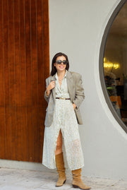 Woman in a patterned dress and gray blazer standing in front of a modern building entrance.