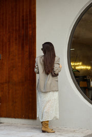 Woman in a beige coat standing in front of a round mirror with a wooden panel.