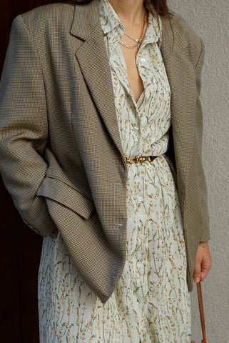 Person wearing a patterned dress with a beige blazer against a neutral background